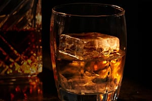 A perfectly clear, large square Hoshizaki ice cube chills a drink in a dimly lit glass tumbler