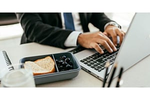 A corporate employee eating lunch while working at a laptop, representing Hoshizaki equipment used in a business office setting