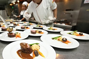 Chefs wearing white gloves are quickly plating gourmet meals at a pass-through station, relying on Hoshizaki refrigeration for ingredient freshness