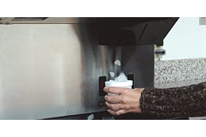 Person dispensing cubed ice into a cup from a stainless steel Hoshizaki commercial ice dispenser