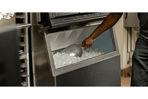 A person using a metal scoop to retrieve ice from a stainless steel Hoshizaki ice storage bin