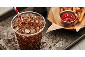 A close-up of a fizzy soda filled with Hoshizaki Cubelet chewable ice and a red and white straw, served next to an order of fries and ketchup on a metal tray