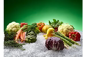 A vibrant display of colorful fresh produce, including cauliflower, peppers, and asparagus, resting on a bed of Hoshizaki flaked ice to maintain market freshness