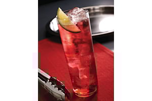 Tall glass of red cocktail garnished with a lime slice and Hoshizaki ice