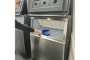 A person scooping Hoshizaki KM Crescent Ice from a stainless steel commercial ice storage bin