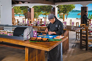 Chef cutting fish at a sushi case display, featuring Hoshizaki refrigerated equipment in an outdoor resort setting
