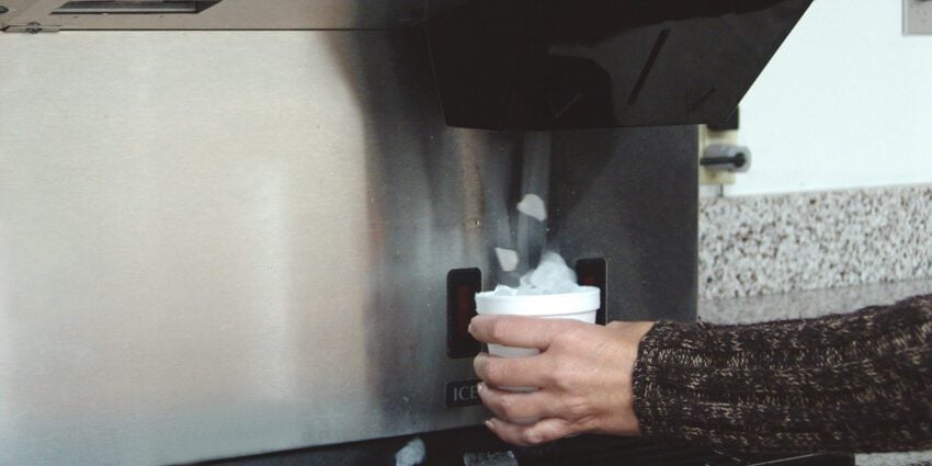 Person dispensing cubed ice into a cup from a stainless steel Hoshizaki commercial ice dispenser
