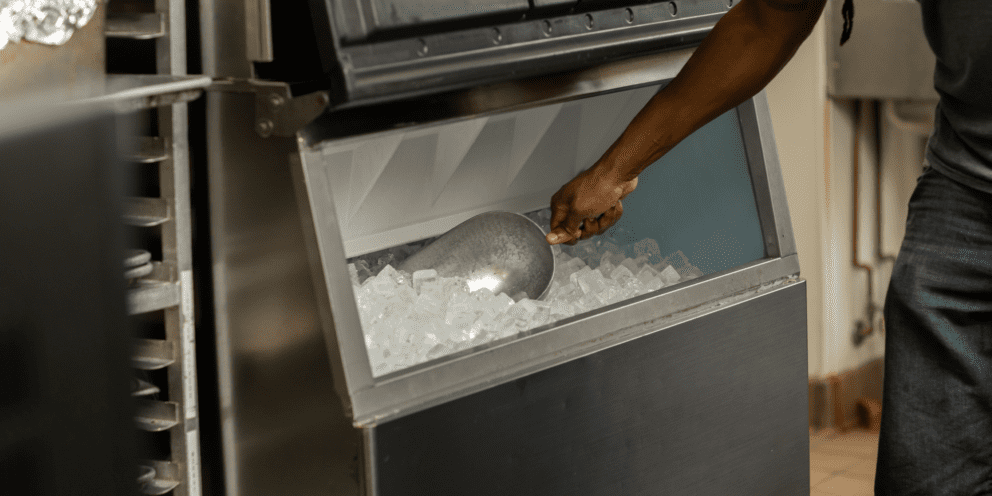 A person using a metal scoop to retrieve ice from a stainless steel Hoshizaki ice storage bin