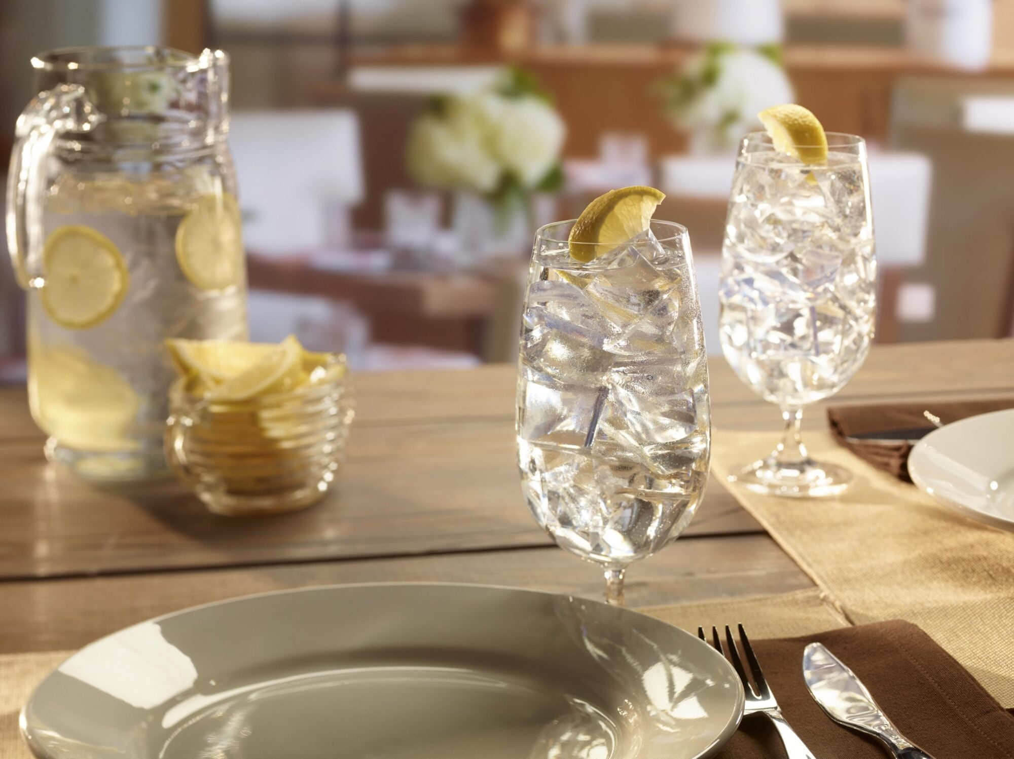 A close-up of a table setting featuring clear glasses of lemon water filled with large, hard Hoshizaki crescent ice, set in a bright, modern restaurant environment