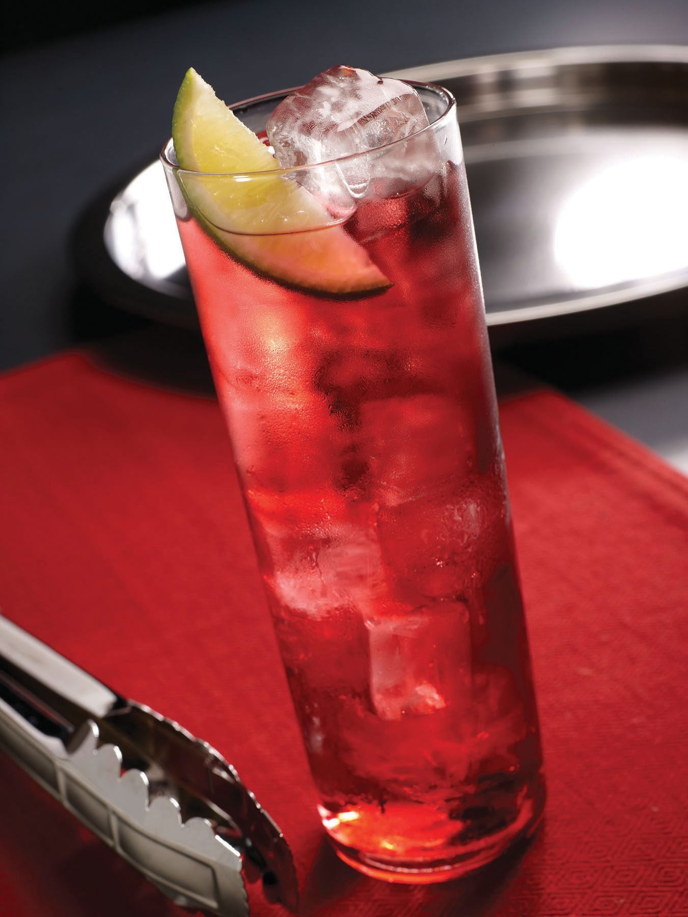 Tall glass of red cocktail garnished with a lime slice and Hoshizaki ice