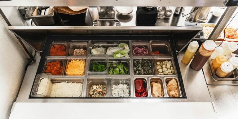 Hoshizaki refrigerated prep table display well stocked with fresh ingredients for food assembly in a fast-casual setting