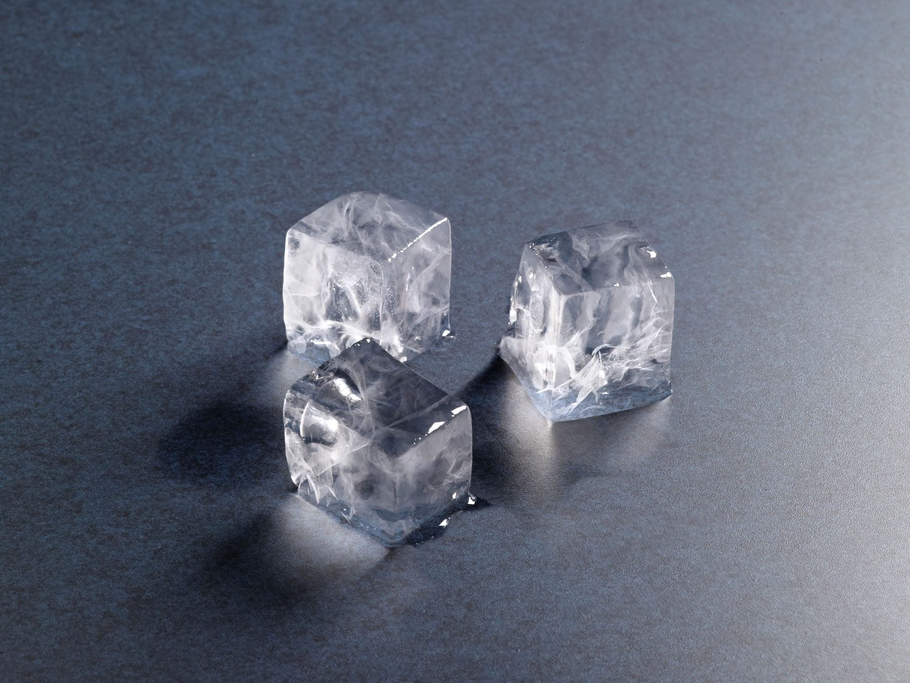 Three clear, square Hoshizaki ice cubes melting on a metallic surface